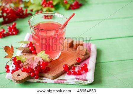 Fresh viburnum drink in glass on green wooden background with leaves and berries. Selective focus.