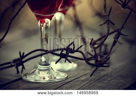 Rusty barbed wire and glasses with red wine on a table. Alcoholic dependence.