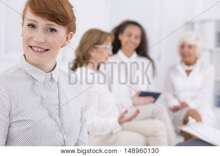 Portrait of red-haired young businesswoman with other woman at the background