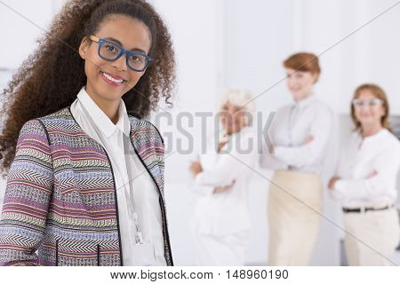 Three white clothed woman standing behind the smiled woman in glasses