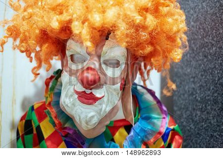 Humeral portrait of mannequin dressed in clown suit, rubber mask and red wig.