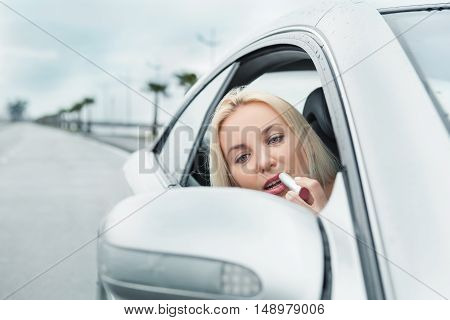 Woman apply rose lipstick looking in car mirror