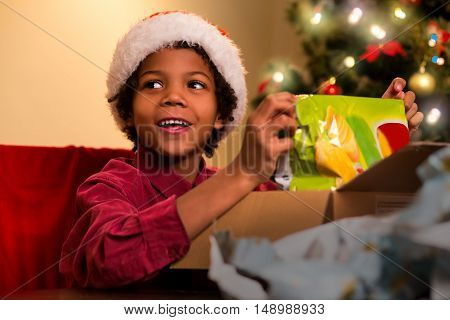 Smiling darkskinned boy unpacks present. Afro kid opens Christmas present. Happiest moment of evening. Holiday for every child.