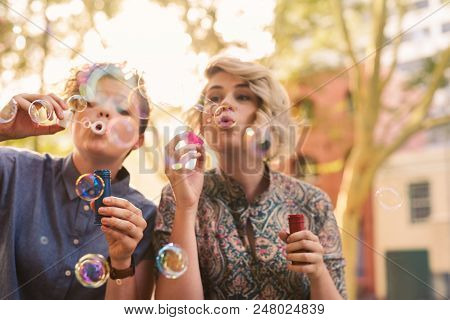 Smiling Young Lesbian Couple Having Fun Blowing Bubbles Together With A Bubble Wand While Enjoying A