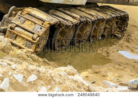 Old Iron Caterpillar In Wet Sand. Rusty Steel Wheels And Caterpillar Tape Of A Large  Bulldozer, Tan