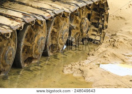 Old Iron Caterpillar In Wet Sand. Rusty Steel Wheels And Caterpillar Tape Of A Large  Bulldozer, Tan