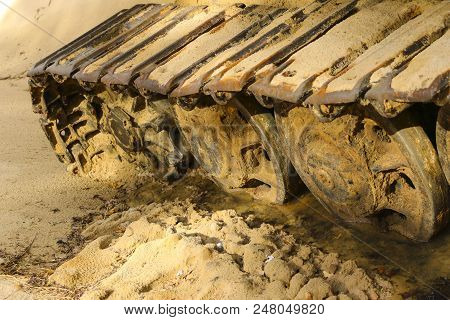 Old Iron Caterpillar In Wet Sand. Rusty Steel Wheels And Caterpillar Tape Of A Large  Bulldozer, Tan