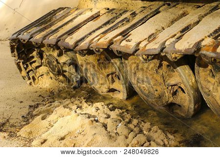 Old Iron Caterpillar In Wet Sand. Rusty Steel Wheels And Caterpillar Tape Of A Large  Bulldozer, Tan