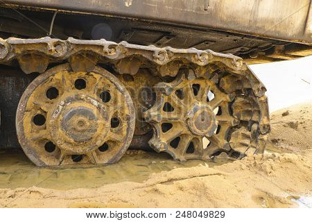 Old Iron Caterpillar In Wet Sand. Rusty Steel Wheels And Caterpillar Tape Of A Large  Bulldozer, Tan