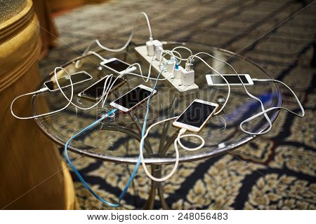 Group Of Smartphones Charging On The Glass Table With Sharing The Same Ac Plug