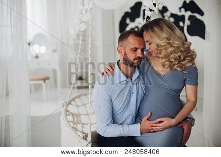 Portrait Of Beautiiful Couple Of Pregnant Woman And Her Husband Sitting And Embracing Each Other, Fa