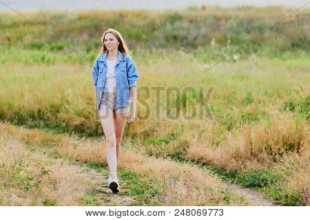 Happy Smiling Young Girl Wearing Blue Jeans Jacket And Shorts Is Standing In The Field