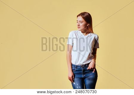 Portrait Of Smiling Beautiful Blonde Girl In White T-shirt And Jeans Against Yellow Background.
