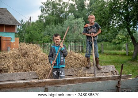 Litynia Village, Ukraine - June 02, 2018: Two Young Boys Throw Hay Out Of A Cart, Stocking Hay For L