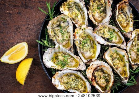 Barbecue overbaked fresh opened oyster with garlic, lemon and herbs offered as top view on a tray 