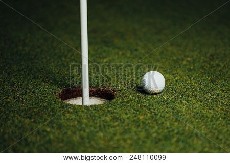 golf ball nearby hole with pin flag, green grass background, closeup view