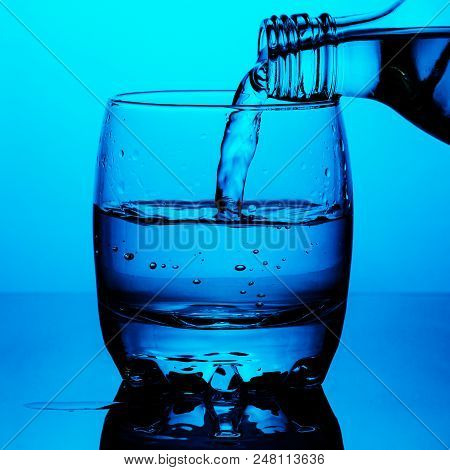 Clean Drinking Water Is Poured From A Bottle A Glass Cup On Blue Background