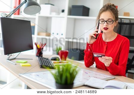 Beautiful Young Girl In Glasses And A Red Shirt Is Working In The Office. Photo With Depth Of Field.