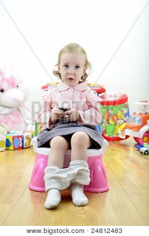 Little Girl Sitting On The Potty With A Remote Control (or Mobile Phone) In Hand