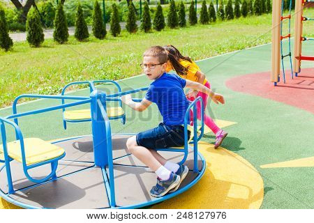 Brother And Sister On The Playground On A Summer Sunny Day Riding A Carousel
