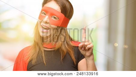 Middle age super hero woman wearing red mask and cape pointing away side with finger