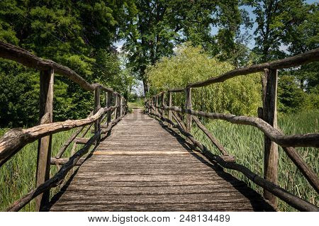 A Narrow Bridge Made Of Wood Leading Over A Wetland Full Of Reed On A Sunny Day In Spring