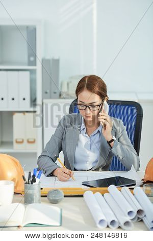 Prefessional Vietnamese Female Engineer Callng On Phone And Correcting Blueprint
