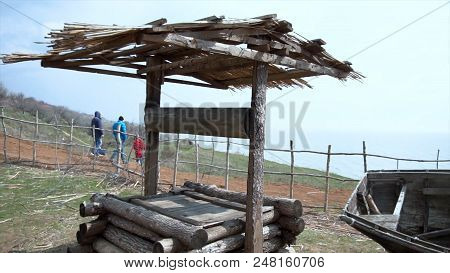 Panoramic View Of Village. Old Dilapidated Black Wooden Boat With A One-storey House, A Well And A H