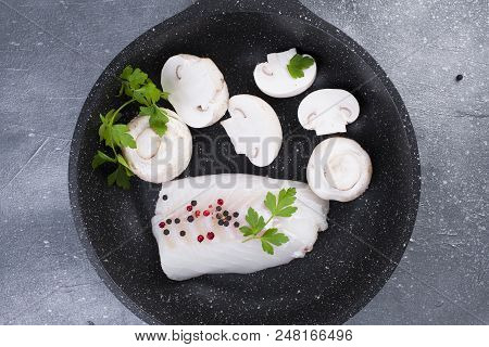 Preparation Of A Seafood Dinner. Fillet Of White Fish In A Black Frying Pan With Mushrooms And Spice