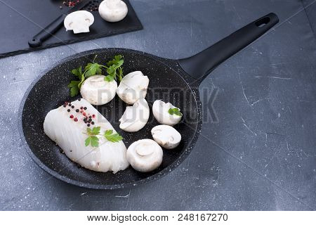 Preparation Of A Seafood Dinner. Fillet Of White Fish In A Black Frying Pan With Mushrooms And Spice