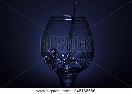 Simple Still-life Photo Of Whisky Glass, Water Jet And Dim Colour Light