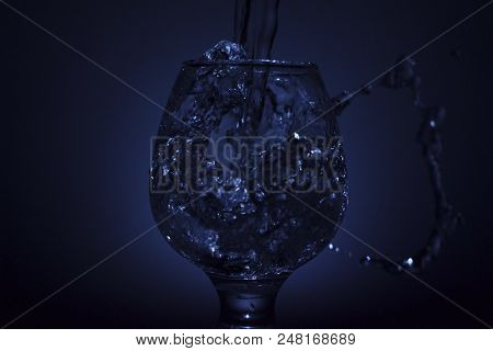 Simple Still-life Photo Of Whisky Glass, Water Jet And Dim Colour Light