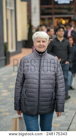 Elderly Woman On The Shopping Streen With A Bag Wearing Winter Clothes