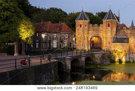 Koppelpoort In Amersfoort In The Evening With Lighted Lamp Posts At The Old Monument.