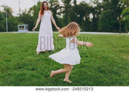 Pretty Little Cute Child Baby Girl In Light Dress Circling Around And Have Fun On Green Grass Lawn I