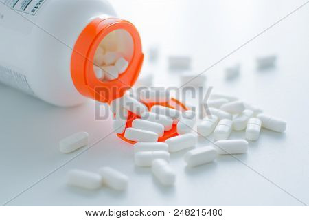 White Tablets Spilling Out Of A Plastic White Bottle With A Tablet