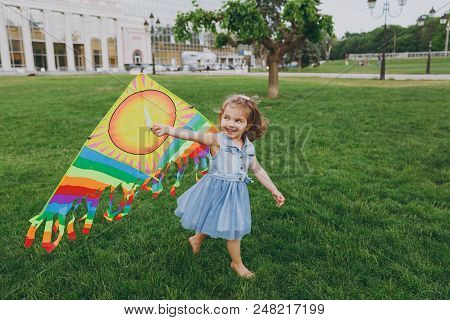 Joyful Little Cute Child Baby Girl In Denim Dress Walking, Play With Colorful Kite And Have Fun In G