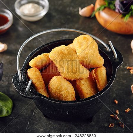 Heap of Delicious Chicken Nuggets in Metal Bowler on Dark Background. Caloric Protein Product Surrounded by Spices. Chicken Fillet in Breading