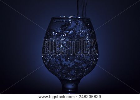 Simple Still-life Photo Of Whisky Glass, Water Jet And Dim Colour Light