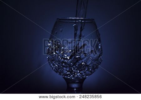 Simple Still-life Photo Of Whisky Glass, Water Jet And Dim Colour Light