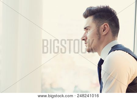 Side View Of Preoccupied Young Man Looking Away In Window With Feeling Of Loneliness.