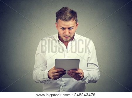 Casual Young Man Watching Tablet With Feeling Of Puzzlement Standing On Gray Background.