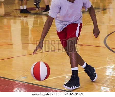 A Young Black Male Is Dribbling A Basketball Indoors During Summer Basketball Camp.