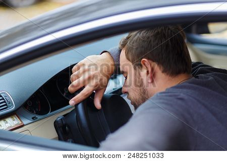 A Tipsy Black-bearded Man Is Lying On A Steering Wheel, Unable To Drive A Car.