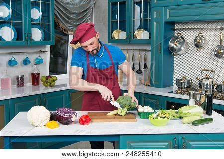 Guy In Apron Preparing Broccoli. Chef Cutting Broccoli At Home Kitchen. A Man Cuts Up Fresh Broccoli