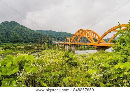 Landscape Of Yellow Arched Railroad Bridge Spanning A River In The Countryside On A Cloudy Overcast 