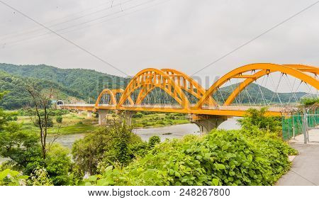 Landscape Of Yellow Arched Railroad Bridge Spanning A River In The Countryside On A Cloudy Overcast 
