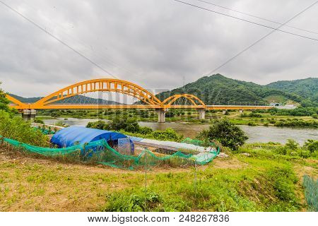 Landscape Of Blue Tent Structure Surrounded By Green Mesh Fence Next To River With Yellow Arched Rai