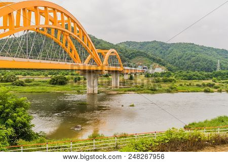 Landscape Of Yellow Arched Railroad Bridge Spanning A River In The Countryside On A Cloudy Overcast 