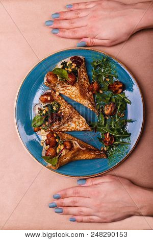 Two Hands Are Lying Near A Blue Plate Full Of Folded Pancakes With Vegetarian Fillings Consisting Of